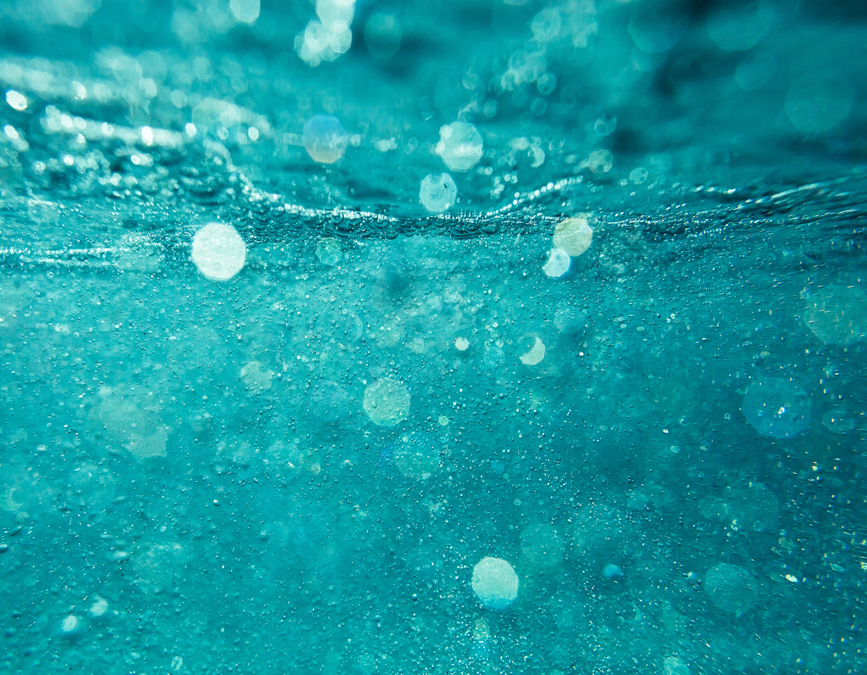 Unterwasseraufnahme im Solebecken mit türkisfarbenem, welligem Wasser und aufsteigenden Luftbläschen.