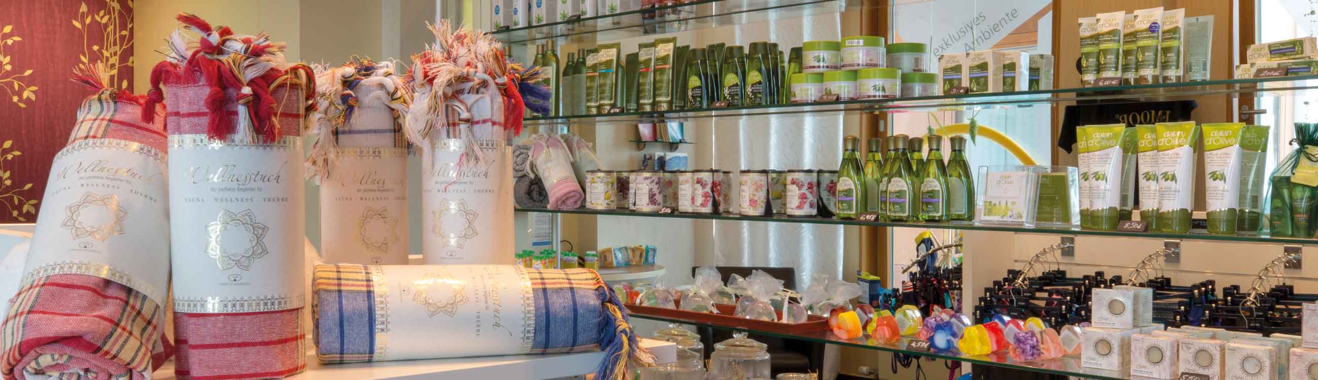 Ausschnitt aus dem Thermeshop der SaarowTherme mit farbigen Hamamtüchern im Vordergrund. Im Hintergrund bunte Seifen und grüne Shampoo-Flaschen.