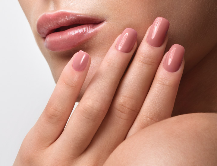 Schön geschminkte Frau hält eine Hand am Gesicht. Die Hand sind gut gepflegt und mit rosafarbenem Nagellack lackiert.