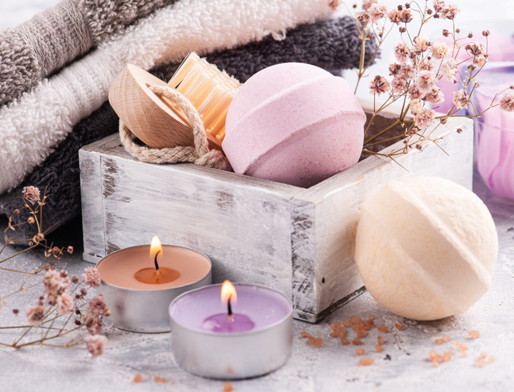 Bunte Badekugeln, kleine bunte Teelichter, zusammengelegte Handtücher und eine Bürste sorgfältig zusammengelegt und präsentiert als Geschenkset.