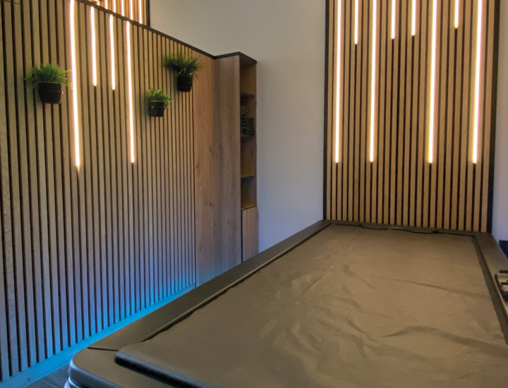 Raum mit Akkustikpanelen und warmen Lichtleisten, blaue Akzentbeleuchtung, Hydrojet-Massageliege mit LED Beleuchtung.