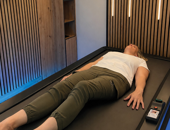Person liegt entspannt auf Hydrojet-Massageliege, warmes Licht in der Massage-Lounge.