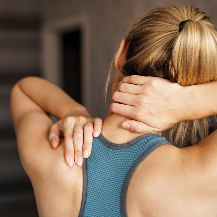 Frau fasst sich an den schmerzenden Nacken, Sporttop, Nahaufnahme von hinten