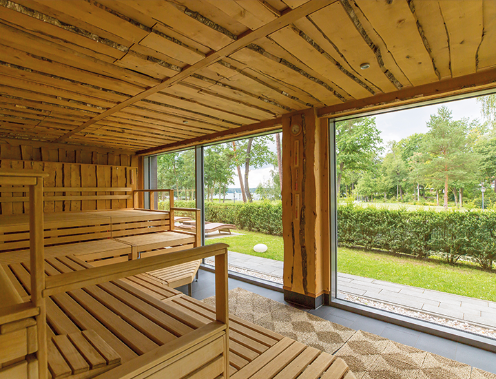Holzsauna mit Stufenbänken und großem Fensterblick ins Grüne.