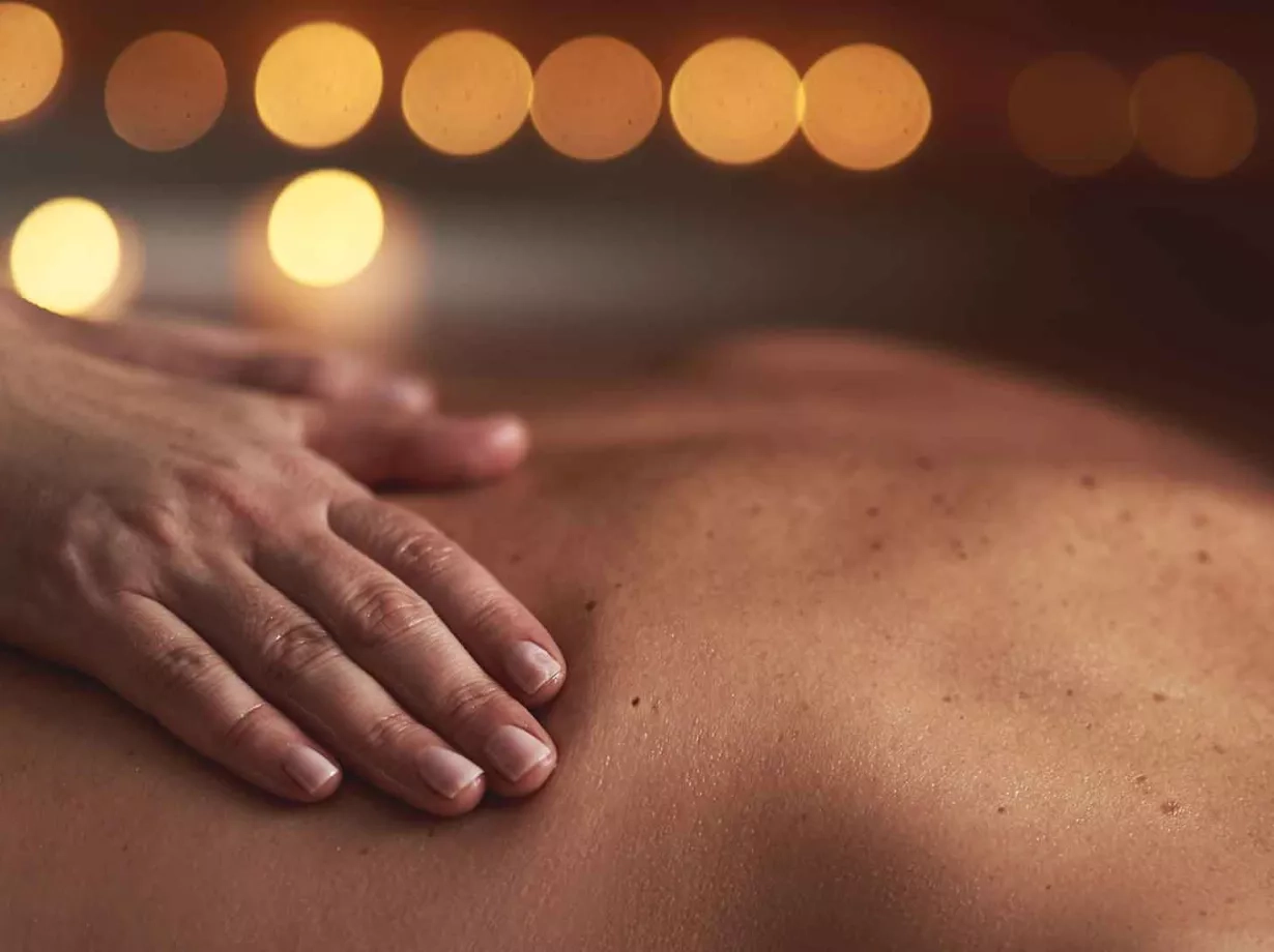 Ein Ausschnitt auf dem zu sehen ist, dass eine Person auf der Brustliegend auf dem Rücken massiert wird. Von der Seite fotografierend und zwei Hände berühren den Rücken.