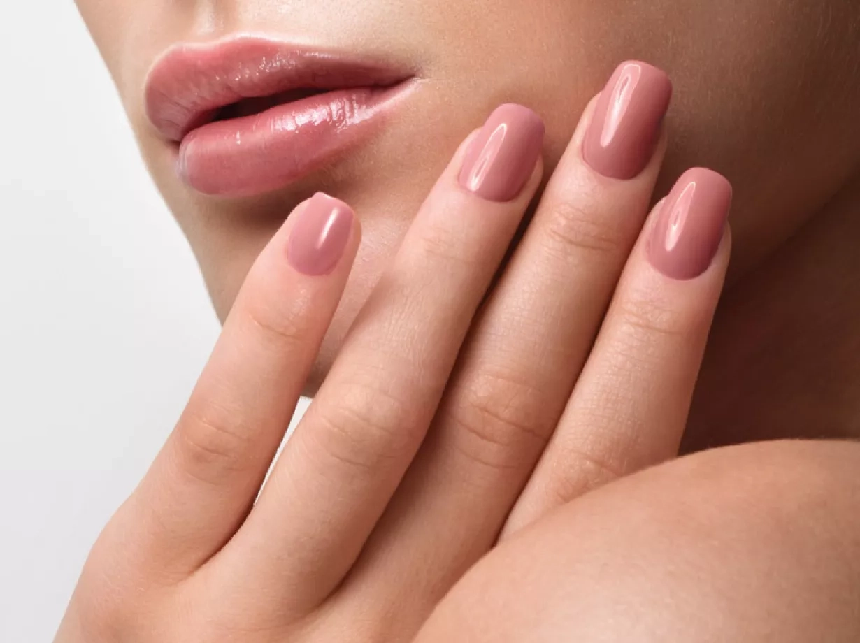 Schön geschminkte Frau hält eine Hand am Gesicht. Die Hand sind gut gepflegt und mit rosafarbenem Nagellack lackiert.