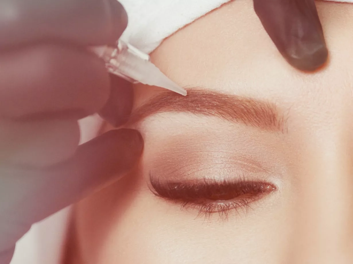 Aufnahme einer lächelnden Frau. Ihre Augenbrauen bekommen eine Behandlung mit Permanentem Make Up.  