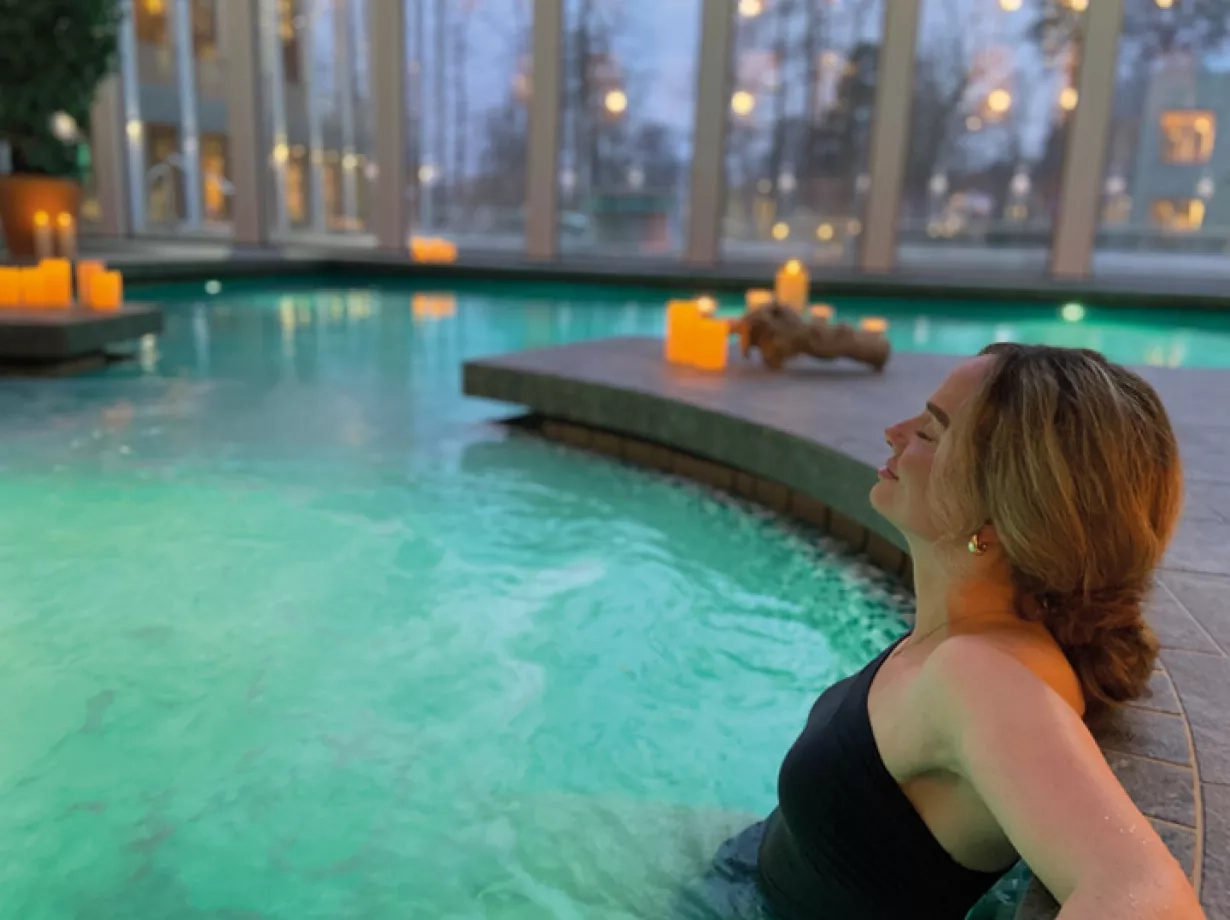 Eine Frau sitzt mit geschlossenen Augen entspannt in einem Whirlpool, umgeben von warmem, sprudelndem Wasser.