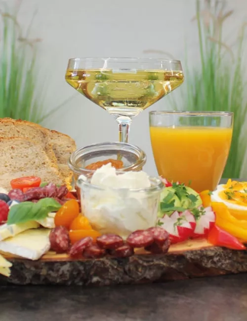 Auf einem Tisch steht ein leckeres Sektfrühstück mit frischem Obst, Käseschnitt, Brotscheiben, frischen Orangensaft, Kaffee und Sekt.