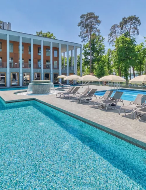 Außenbereich der SaarowTherme mit Thermalsolebecken, Strömungskanal und Sonnenliegen. Entspannende Atmosphäre unter blauem Himmel.