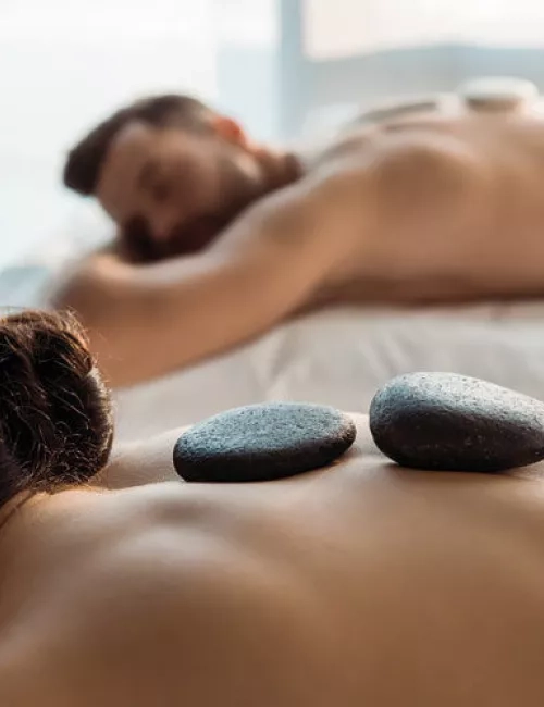 Ein Paar liegt entspannt nebeneinander bei einer Hot-Stone-Massage in ruhiger Atmosphäre.