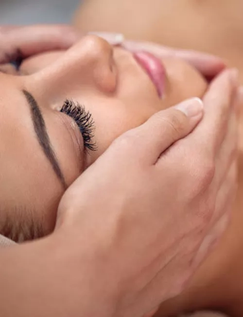 Eine Frau mit geschlossenen Augen genießt eine beruhigende Gesichtsmassage, während ihr Kopf sanft von Händen gehalten wird.