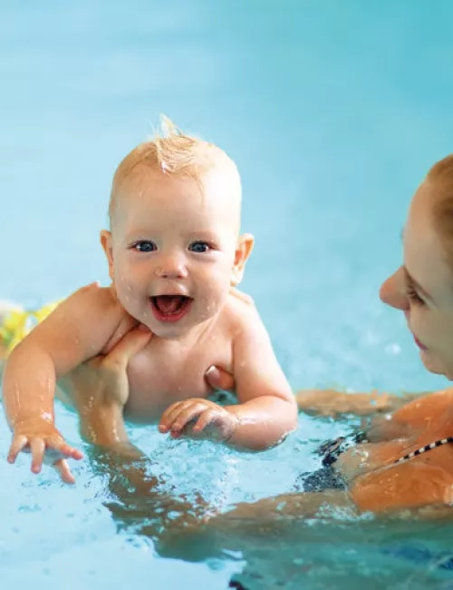 Ein glückliches Baby wird von einer Frau im Schwimmbad gehalten und lacht fröhlich im Wasser.