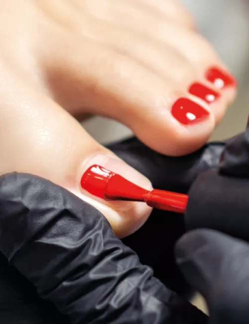 Fußpflege-Behandlung an den Zehennägeln mit rotem Nagellack.
