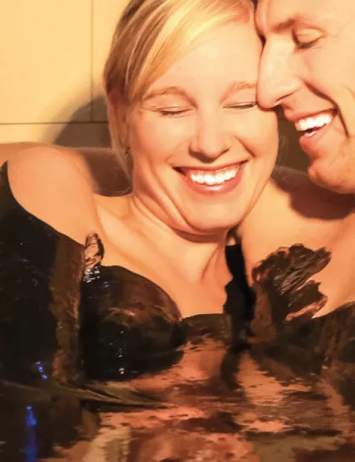 Lachendes Paar genießt gemeinsam ein wohltuendes Moorbad in entspannter Atmosphäre.