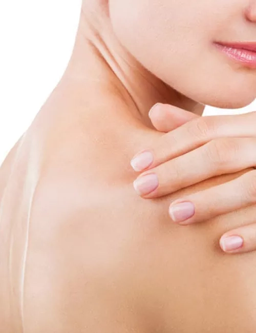 Eine Frau berührt sanft ihre Schulter und zeigt dabei glatte, gepflegte Haut.