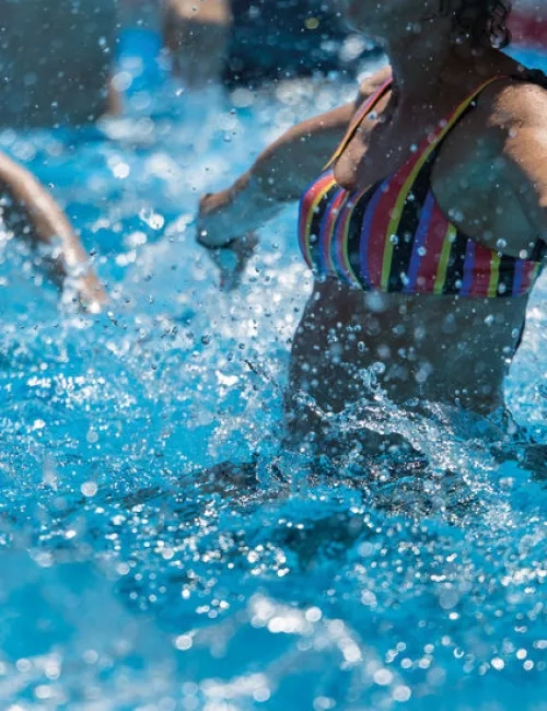 Mehrere Personen bewegen sich im Wasser eines Pools, Wasser spritzt.