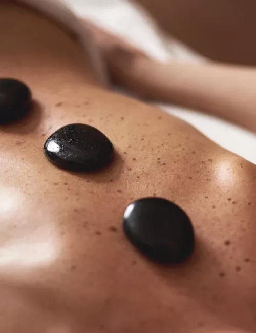 Glatte schwarze Massagesteine liegen auf dem Rücken einer Person während einer Hot-Stone-Behandlung.