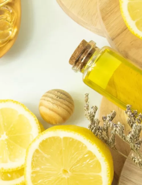 Arrangement aus Naturkosmetik-Zutaten: eine aufgeschnittene Zitrone, Massagekugeln aus Holz, ein Glas mit gelbem Öl, getrocknete Lavendelzweige und weitere Naturprodukte auf runden Holzunterlagen.