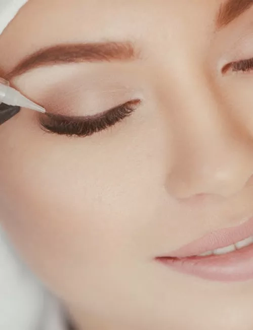 Frau mit geschlossenen Augen erhält ein dauerhaftes Augen-Make-up mit einem feinen Pigmentiergerät am oberen Lidrand.