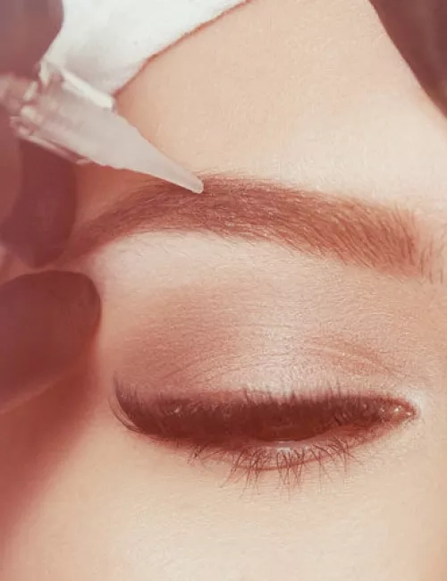 Aufnahme einer lächelnden Frau. Ihre Augenbrauen bekommen eine Behandlung mit Permanentem Make Up.