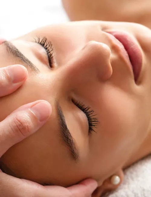 Eine Frau mit geschlossenen Augen erhält eine entspannende Stirnmassage in ruhiger Atmosphäre.