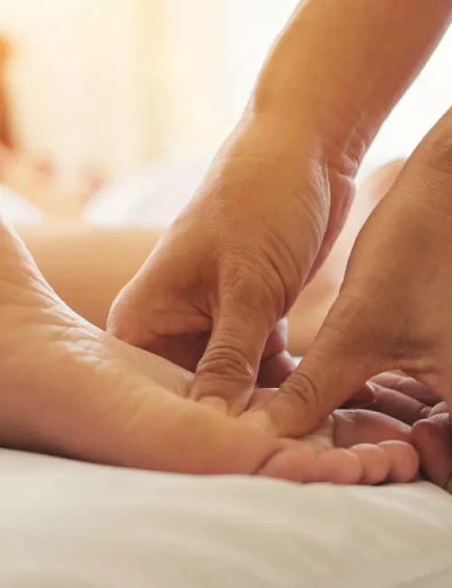 Nahaufnahme einer wohltuenden Fußmassage in entspannter Atmosphäre mit warmem Licht.
