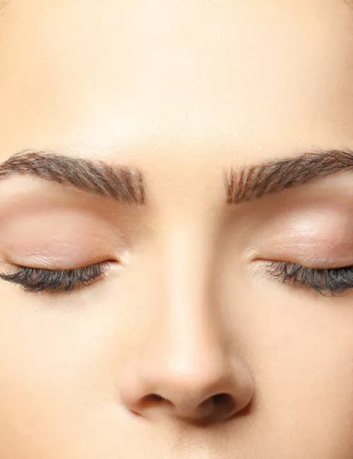 Nahaufnahme eines weiblichen Gesichts mit geschlossenen Augen, perfekt gestylten Augenbrauen und dezentem Make-up, Fokus auf der Augenpartie.