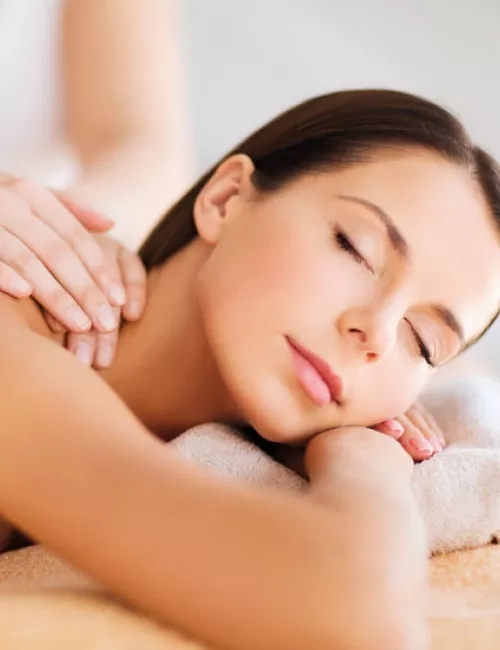 Eine Frau liegt entspannt mit geschlossenen Augen auf einer Massageliege, während eine Therapeutin ihr den Rücken massiert.