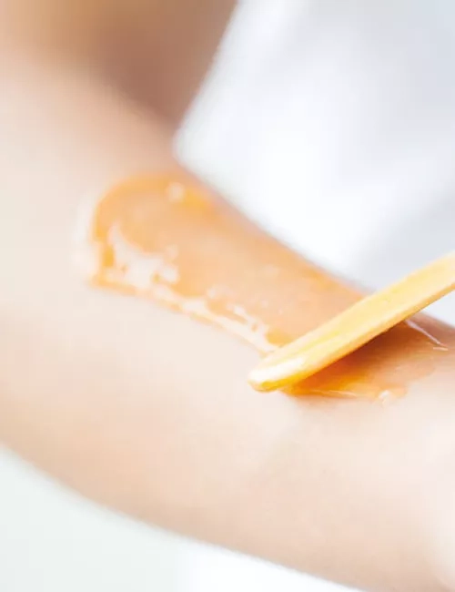 Auftragen von warmem Wachs auf einen Unterarm mit einem Holzspatel zur Haarentfernung.