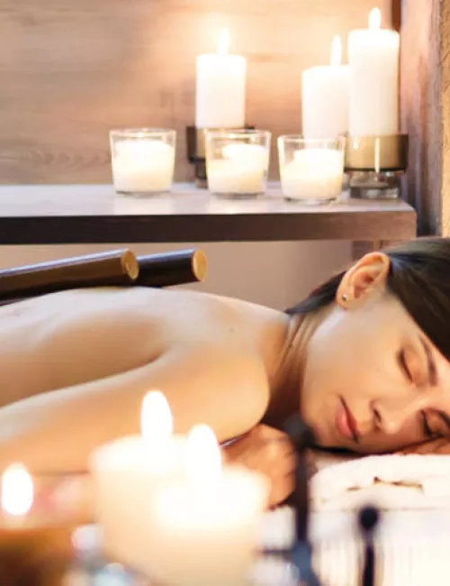 Eine Frau mit dunkelbraunen Haaren liegt entspannt bei einer Wellnessbehandlung mit Bambusstäben, umgeben von warmem Kerzenlicht.