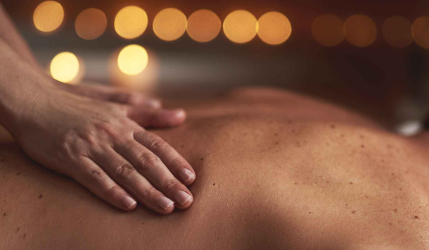 Ein Ausschnitt auf dem zu sehen ist, dass eine Person auf der Brustliegend auf dem Rücken massiert wird. Von der Seite fotografierend und zwei Hände berühren den Rücken.