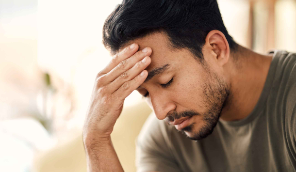 Ein Mann mit kurzen schwarzen Haaren, Bart trägt ein Olivenfarbenes T-Shirt und stützt seinen Kopf auf seine Fingerkuppen ab und hat dabei die Augen geschlossen.