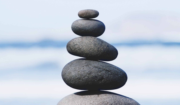 Bild von dunkelgrauen Steinen die in einer Linie gestapelt sind als Steinmännchen.