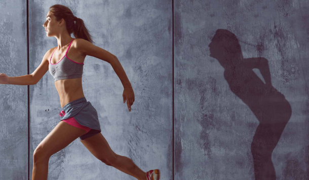 Aufnahme einer jungen Frau in Sportbekleidung, die von Ihrem Schatten wegläuft. Ihr Schatten steht still, gebeugt nach vorne und Sie hält Ihre Hand vor Schmerzen am Rücken. 
