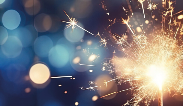 Ein Bild von einer Wunderkerze die schön leuchtet. Im Hintergrund ganz viele funkelnde Lichter. 