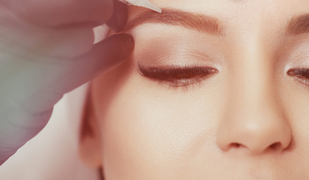 Aufnahme einer lächelnden Frau. Ihre Augenbrauen bekommen eine Behandlung mit Permanentem Make Up.  