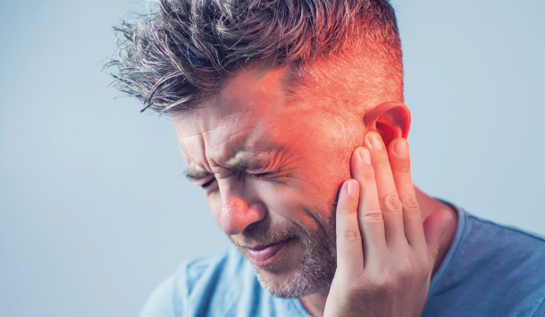 Junger Mann hält eine Hand am Ohr. Er Verzieht vor Schmerz sein Gesicht und am Kopf ist rund um seinem Ohr eine rote Farbe, die den Schmerzbereich verdeutlichen soll.