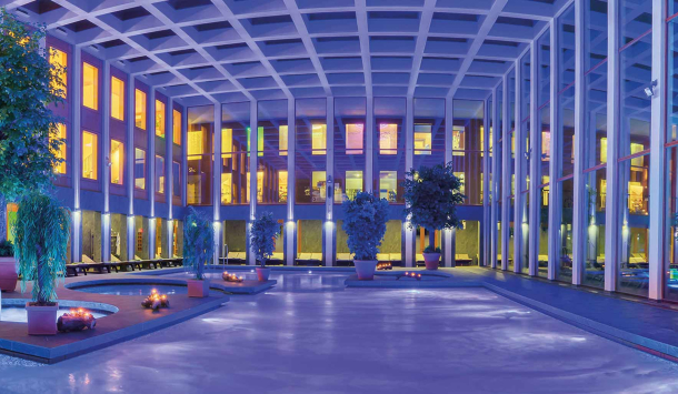 Thermalbad der SaarowTherme in einem blauen und lila Licht getaucht. Kerzenschein am Beckenrand sorgt für eine romantische Stimmung im Bad.