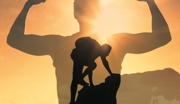 Aufnahme eines Mannes, der an die Spitze eines Berges angekommen ist. Er hat den Berg erfolgreich bestiegen und im Hintergrund scheint die Sonne. Im Vordergrund ist abgebildet wie sein Schatten vor lauter Freude die Arme seitlich hochhält und dabei seine Muskeln anspannt.