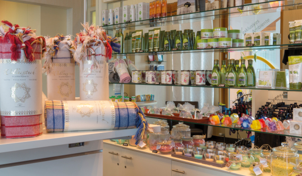 Ausschnitt aus dem Thermeshop der SaarowTherme mit farbigen Hamamtüchern im Vordergrund. Im Hintergrund bunte Seifen und grüne Shampoo-Flaschen.