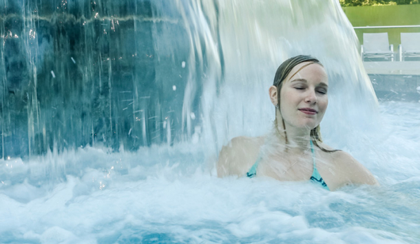 Frau steht unter einem Strömungspilz in der SaarowTherme, Wasser massiert ihre Schulter, sie schließt die Augen und genießt den entspannenden Moment.