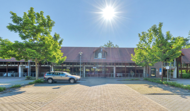 Sonniger Campusplatz mit gepflastertem Weg, Flachbau und grünen Bäumen
