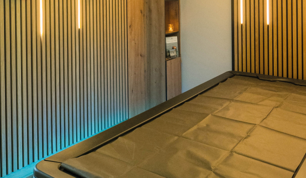 Leerer Innenraum mit Hydrojet-Massageliege, Akustikpanele an den Wänden und warmen Lichtleisten an den Wänden.