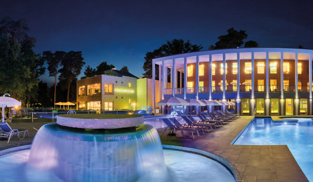 Beleuchtete Aussenbecken der SaarowTherme bei Nacht mit Liegestühlen und modernem Gebäudekomplex.