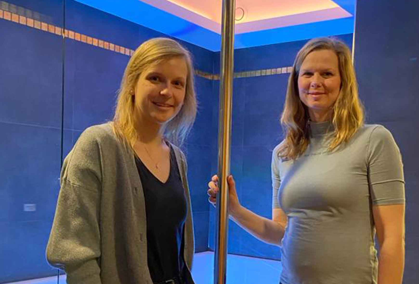 Zwei lächelnde Frauen stehen nebeneinander in einem modern beleuchteten Raum mit blauer Wand und LED-Lichtleisten.