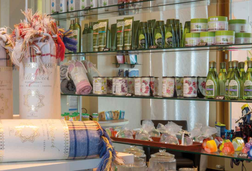 Ausschnitt aus dem Thermeshop der SaarowTherme mit farbigen Hamamtüchern im Vordergrund. Im Hintergrund bunte Seifen und grüne Shampoo-Flaschen.