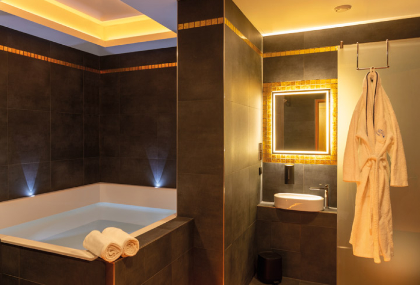 Modern gestaltender Floatingraum in SaarowTherme mit großer Floating-Wanne, beleuchtetem Spiegel über einem Waschbecken und einem aufgehängten Bademantel. Stimmungsvolle Lichtakzente schaffen eine entspannte Atmosphäre.