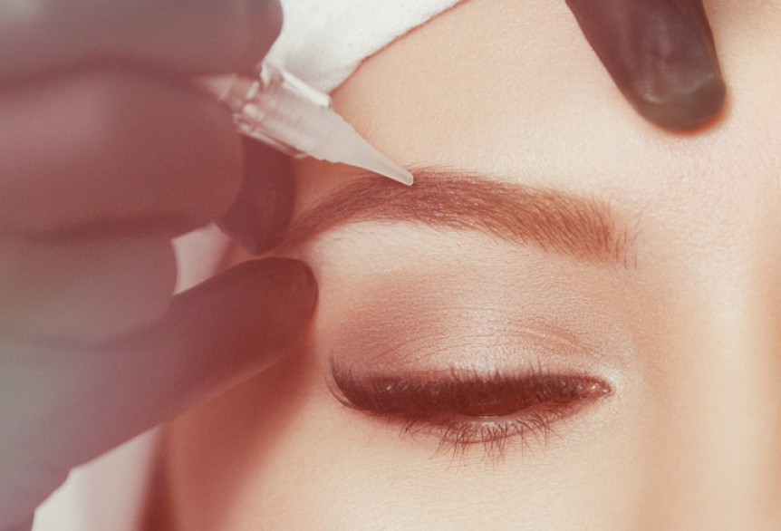 Aufnahme einer lächelnden Frau. Ihre Augenbrauen bekommen eine Behandlung mit Permanentem Make Up.  