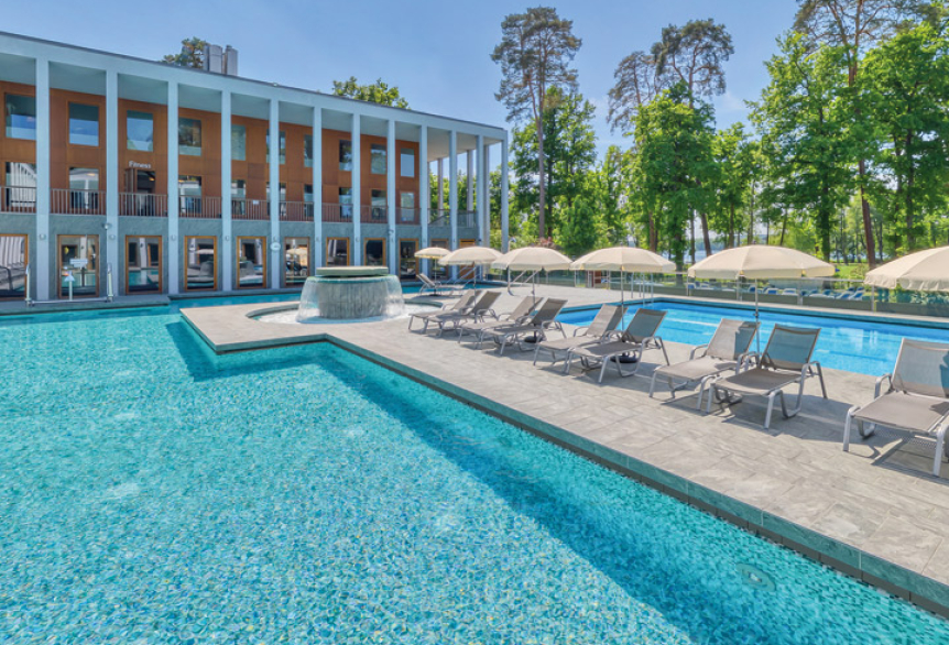 Außenbereich der SaarowTherme mit Thermalsolebecken, Strömungskanal und Sonnenliegen. Entspannende Atmosphäre unter blauem Himmel.